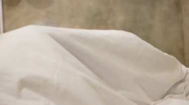 Genç anne ve kızları yatak odasında peekaboo oynayarak eğleniyorlar. Mutlu aile yatakta beyaz battaniyenin altında oynuyor. Mutlu aile ve çocukluk kavramı.