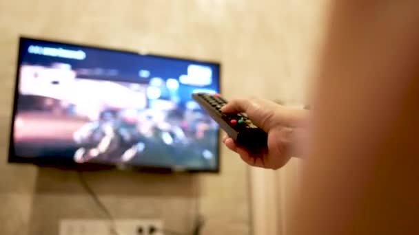 部屋でテレビを見ているアジアの若い女性は 音量を調節したり テレビチャンネルを変更したりするために手をリモートコントロールしています リビングルームでのリラクゼーション 選択的焦点 — ストック動画