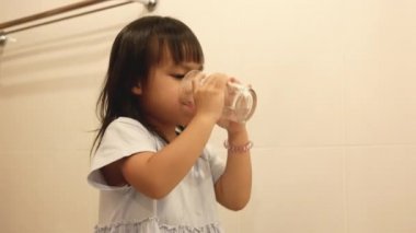 Küçük mutlu kız dişlerini fırçalıyor ve banyoda suyla ağız temizliyor. Ağız temizliği kavramı.