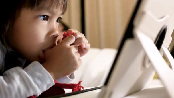 Adorabile Bambina Sdraiata Sul Letto Con Succhiare Pollice Guardando Tablet — Video Stock