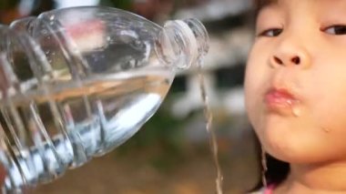 Abur cubur yedikten sonra şişeden su içen sevimli küçük kız gülümseyip parktaki kameraya bakıyor. Mutlu aile ve çocukluk kavramı.