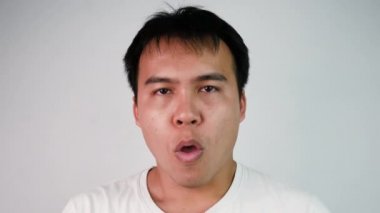 Beyaz tişörtlü, öksüren ve gri arka planda boğaz ağrısı çeken Asyalı hasta adamın portresini yakından çek. Grip belirtileri gösteren bir erkek.. 