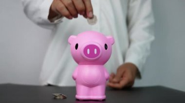 Kadın eli, odadaki pembe domuz kumbarasına bozuk para atıyor. Para kavramı kaydet.