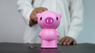 Kadın eli, odadaki pembe domuz kumbarasına bozuk para atıyor. Para kavramı kaydet.