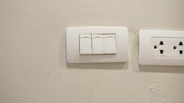 Kadın elinin ya da parmaklarının ıslak olduğu yakın plan beyaz ışık düğmesini kapatıyor. Elektrik tasarrufu. Elektriği ıslak elle ve güvenlikle kullanmama kavramı.