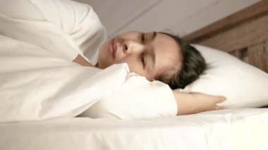 Yorgun Asyalı kadın beyaz bir battaniyeyle kaplanmış tatil gününde yatakta yatıyor..