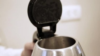 Bir insanın elinin yakın plan çekimi mutfaktaki elektrikli su ısıtıcısına su döküyor..