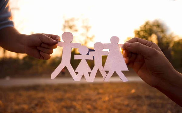 Hands of mother and daughter holding family cut out paper in autumn park on sunset background.