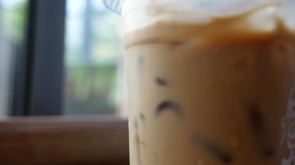 Gros plan de la main de la jeune femme remuer la glace dans une tasse à café en plastique à la paille pour se détendre dans le café pendant les vacances .
