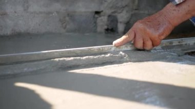 İnşaat işçisi veya sıva işçisi zemine beton döker ve pürüzsüz olması için beton zemini yerle bir eder. İnşaat konsepti.