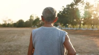 Asyalı son sınıf öğrencisi gün batımında gökyüzü arka planında parkta koşuyor. Sağlıklı yaşam tarzı ve sağlık hizmeti kavramı.