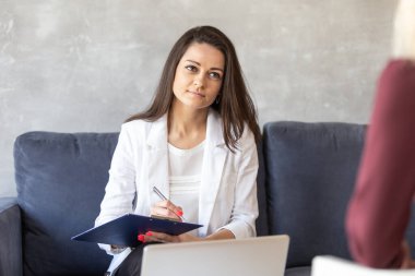 Ciddi bir iş kadını tableti elinde tutuyor ve kağıda notlar yazıyor.