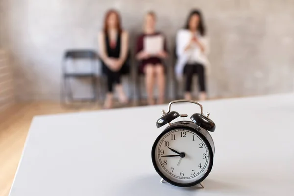Closeup of mechanical clocks on table in office. Three women sits in chair on background. Selective focus