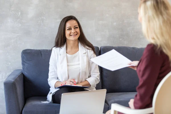 Cute woman smiles to woman with sheet of paper in hands in front of her. Selective focus — Stock Photo, Image