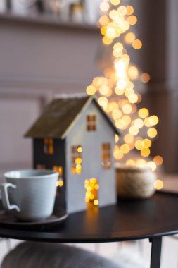 Yakın çekim bulanık fotoğraf. Yılbaşı dekoratif evi ve siyah masanın üzerinde duran iki fincan ışığı.