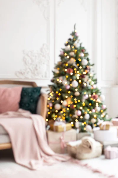 Μπλε φωτογραφία διακοσμημένο με γιρλάντα και παιχνίδια χριστουγεννιάτικο δέντρο στέκεται δίπλα σε λευκό καναπέ. — Φωτογραφία Αρχείου