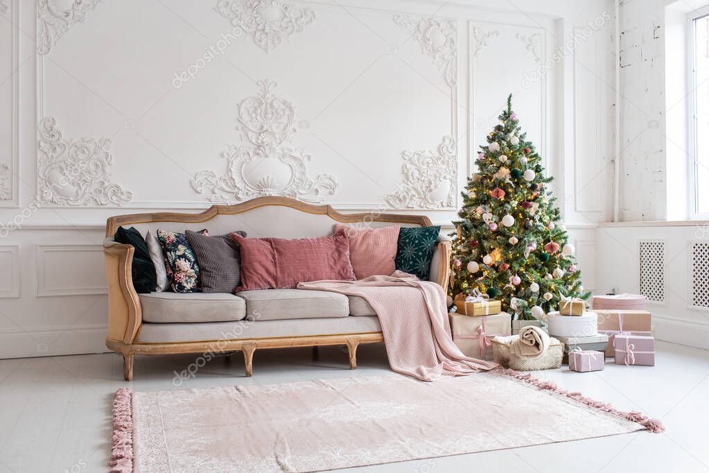 Christmas tree surrounded by giftboxes stands close to sofa in living room
