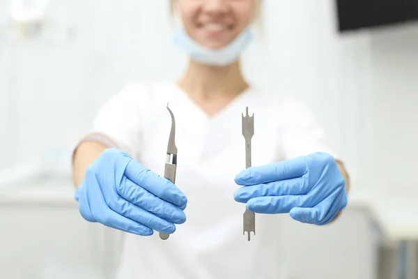 Attractive female dentist holds tools in her hands and smile charmingly. Selective focus — Stock Photo, Image