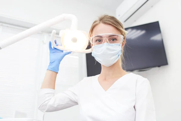 Woman dentist in mask moves lighter lamp closer to patient. Selective focus — Stock Photo, Image