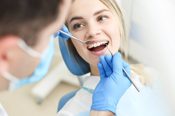 Cute woman sits in dentist chair while dentist examine her teeths. Selective focus