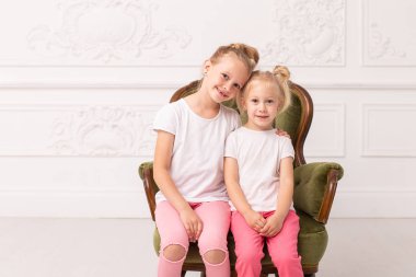 İki küçük sarışın yeşil koltukta oturup birbirlerine sarılırlar.