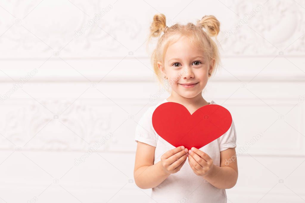 Little adorable girl holds little red heart made of papper in hands