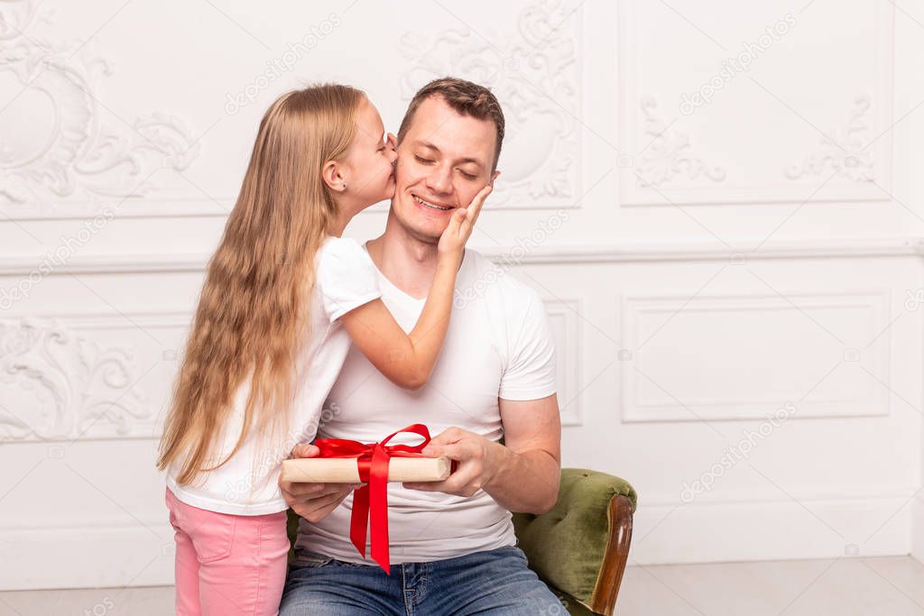 Little girl kiss her father, who hold giftbox in hand, in cheek. Selective focus