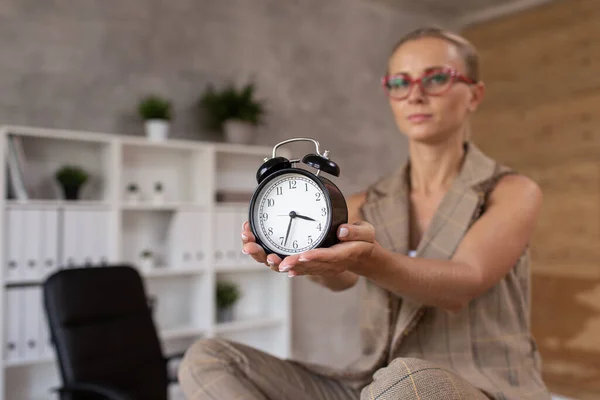 Mujer adulta en gafas se sienta en pose de loto y sostiene los relojes en las manos. Enfoque selectivo — Foto de Stock