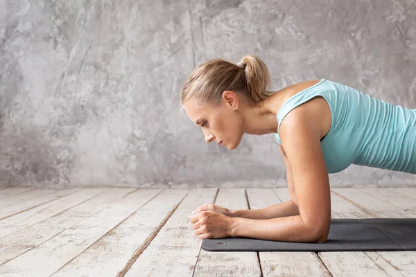 Spor elbiseli, sarışın, tatlı bir kadın. Sırtını tahtada eğitiyor.