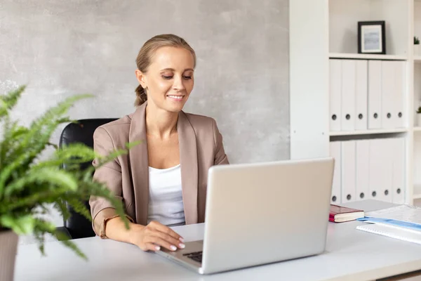 Mujer sonriente se sienta en la oficina y mirando la pantalla de los portátiles — Foto de Stock