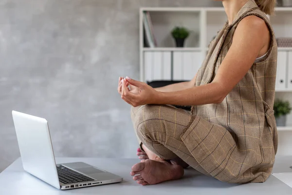 Vuxen kvinna i glasögon sitter på bordet och gör yoga — Stockfoto