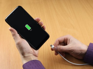 Adam akıllı telefondan şarj kablosunu kesti. Ekranda tam yük görünüyor