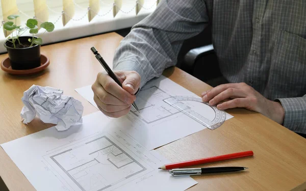 Hands close-up. Person makes notes in the architectural floor plan. View of a working office desk with papers and pencils