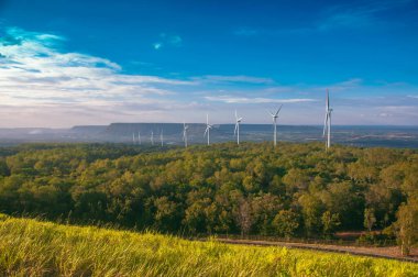 Yeşil ormanlı yel değirmeninin manzarası ve dağın üzerinde açık mavi gökyüzü..