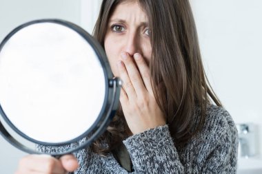 Dissatisfied cute girl looks in the mirror with scared look.