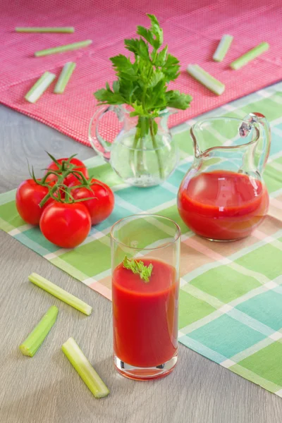 El vaso con el jugo de tomate, los tomates, los tallos y las hojas del apio a la mesa —  Fotos de Stock