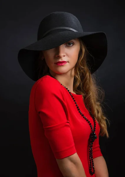 Krásná mladá dívka v zářivě červené šaty a černý klobouk s širokou poli — Stock fotografie