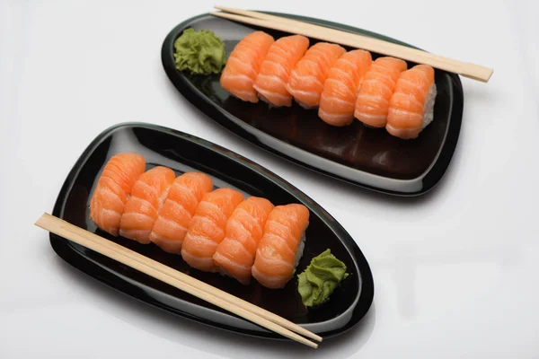 Sushi de salmón, palos de madera y wasabi en dos platos de cerámica negra en forma de frijol Imagen De Stock