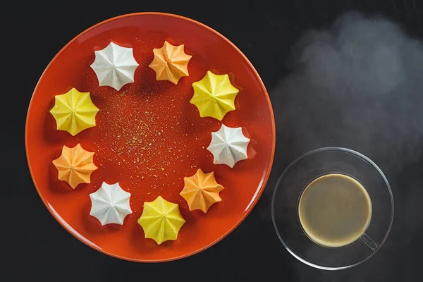 Biscuits figurés multicolores sur une assiette ronde orange et une tasse de café chaud sur un fond noir — Photo