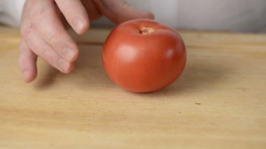 Adam sulu kırmızı domates dilimleri ile büyük tablo bıçak kesiyor