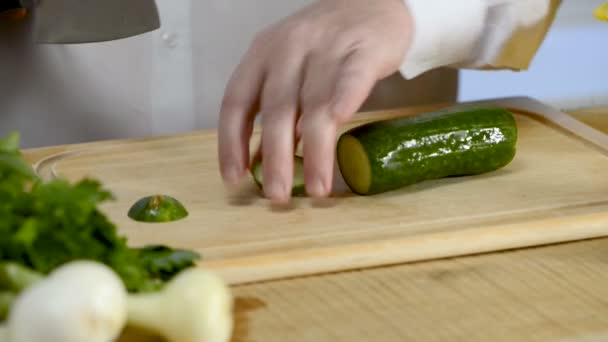 As mãos da faca de cozinheiro grande cozinha um pepino verde fresco em uma tábua de corte de uma árvore — Vídeo de Stock