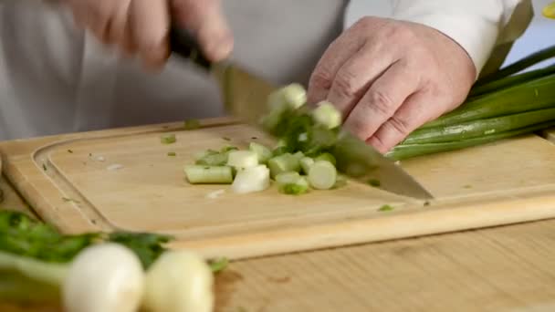As mãos da faca de cozinha grande uma cebola de pena verde fresca em uma tábua de corte de uma árvore — Vídeo de Stock