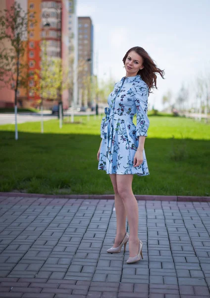 The beautiful girl in a blue short dress costs against the background of the street per windy sunny day — Stock Photo, Image