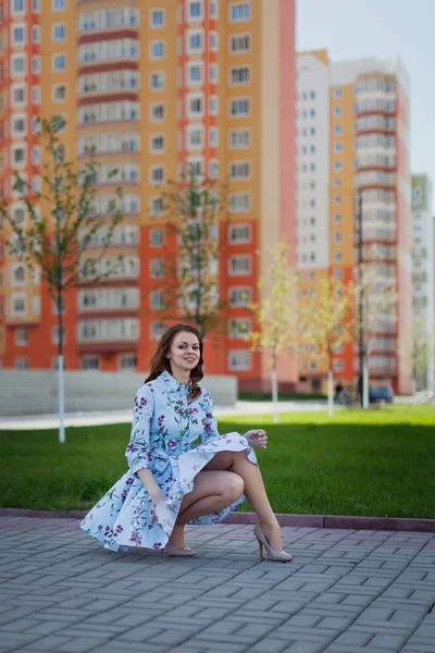 Красивая девушка сидит в синем коротком платье, поднятом ветром на фоне высоких домов — стоковое фото