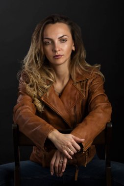 Açık kahverengi deri ceketli, uzun sarı saçlı hoş bir genç kadın.