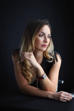 Uzun sarı saçlı, küçük siyah elbiseli, kolsuz, çok seksi bir genç kadın.