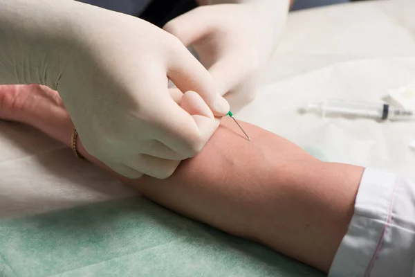 As mãos em luvas médicas realizam punção venosa na área de dobra ulnar da mão do paciente. — Fotografia de Stock