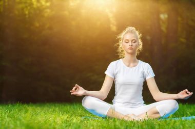 Genç ve güzel bir kadın dışarıda meditasyon yapıyor.