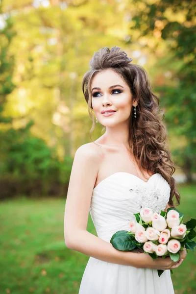 屋外でポーズの花を持つ美しい若い花嫁 — ストック写真