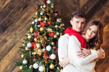 kucaklayan Noel ışıkları arka plan üzerinde poz genç mutlu çift beyaz kazak ve kırmızı eşarp